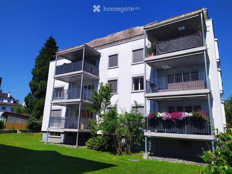 White apartment building with multiple balconies, green lawn, and plants