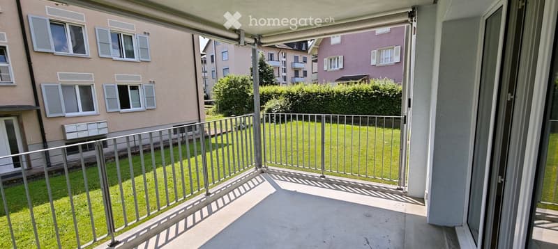Balcony with metal railing overlooking a green lawn and neighboring buildings with shutters and windows.