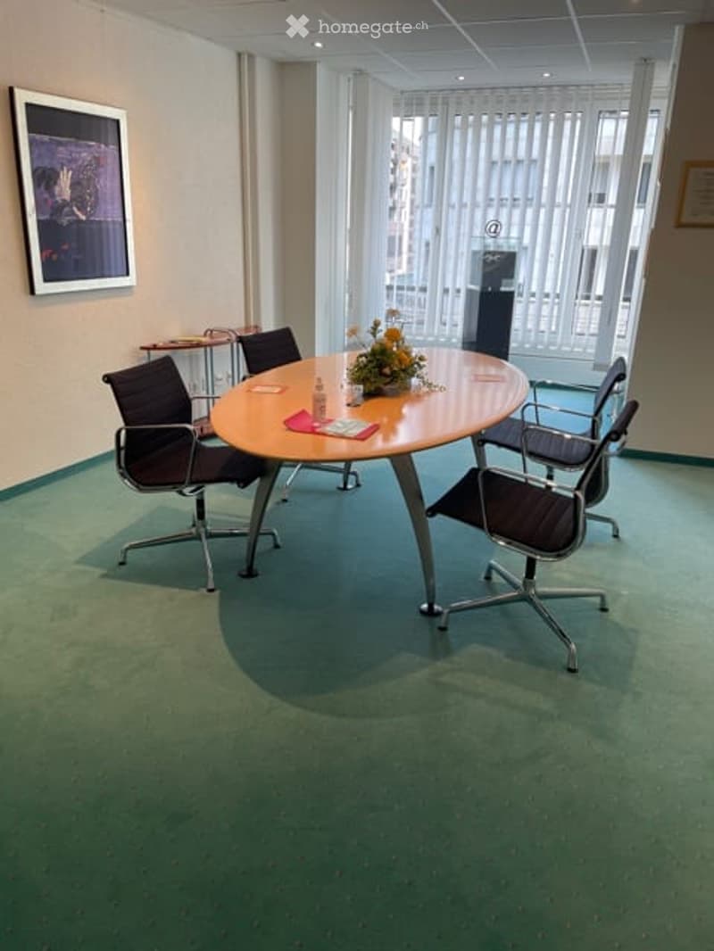 large room, oval table, green carpet, chairs around the table, picture on wall, flower arrangement on the table