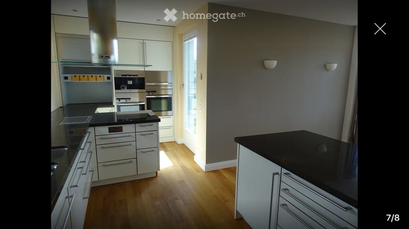 Modern kitchen with white cabinets, stainless steel appliances, black countertops, and wooden flooring.
