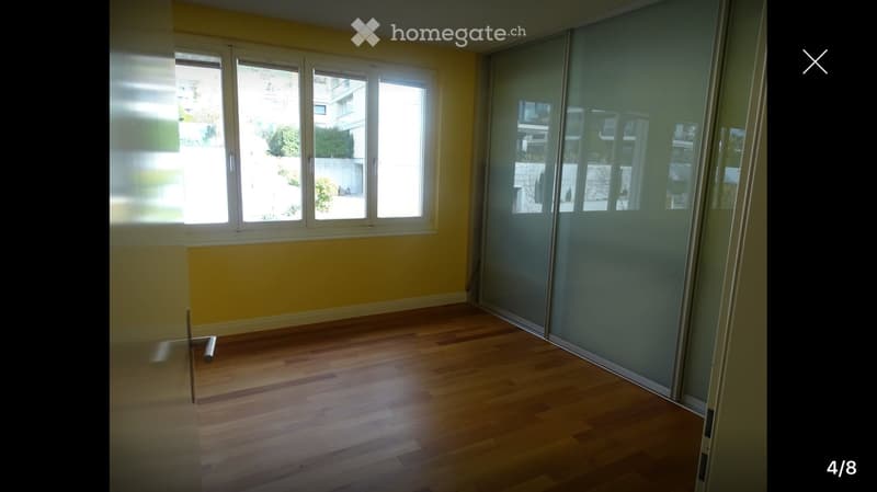 Empty room with wooden flooring, large windows, and a sliding glass door leading to a balcony.