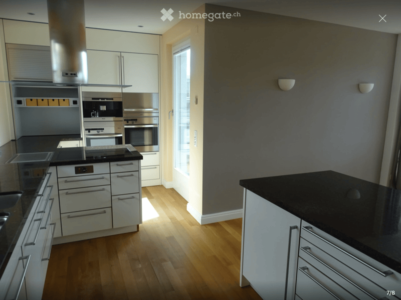 Modern kitchen with white cabinets, stainless steel appliances, black countertops, and wooden flooring.
