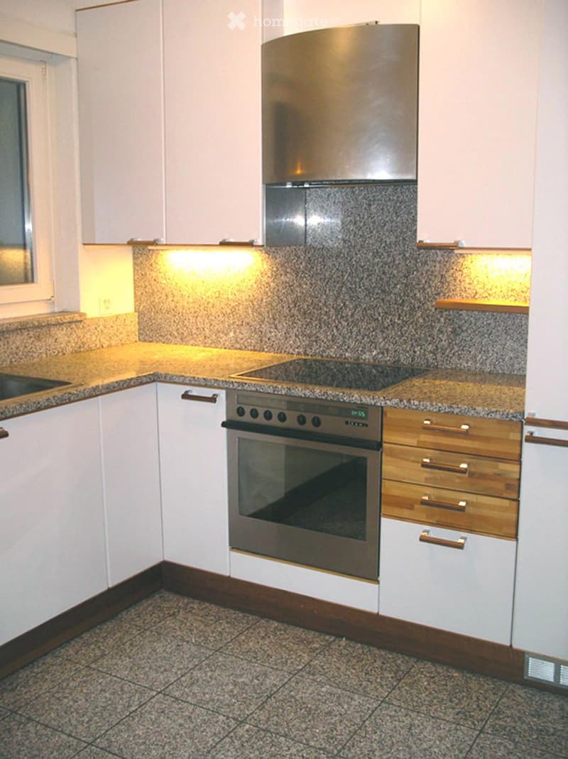 Modern kitchen with white cabinets, granite countertops, stainless steel appliances, and built-in lighting.