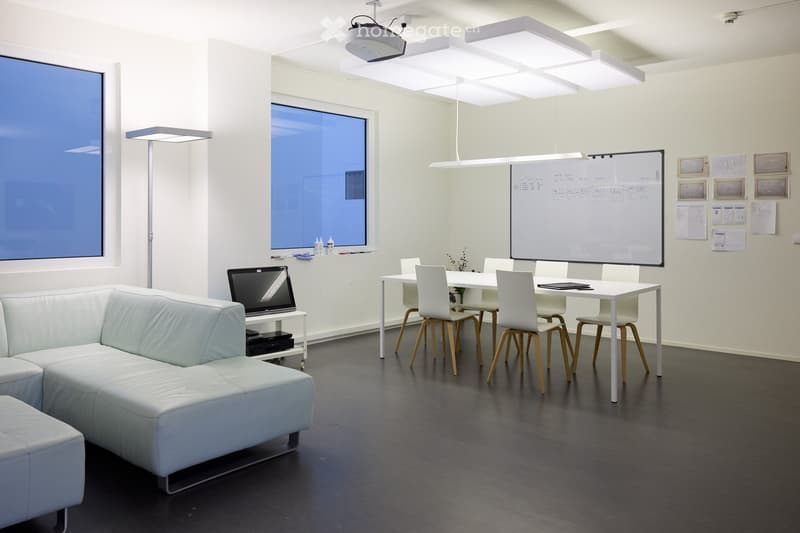 modern office space with white walls, dark grey floor, two large windows, table with six chairs, two sofas, floor lamp, overhead lighting, whiteboard