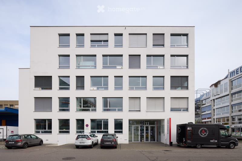 White building with many windows, glass entrance, several parked cars in front