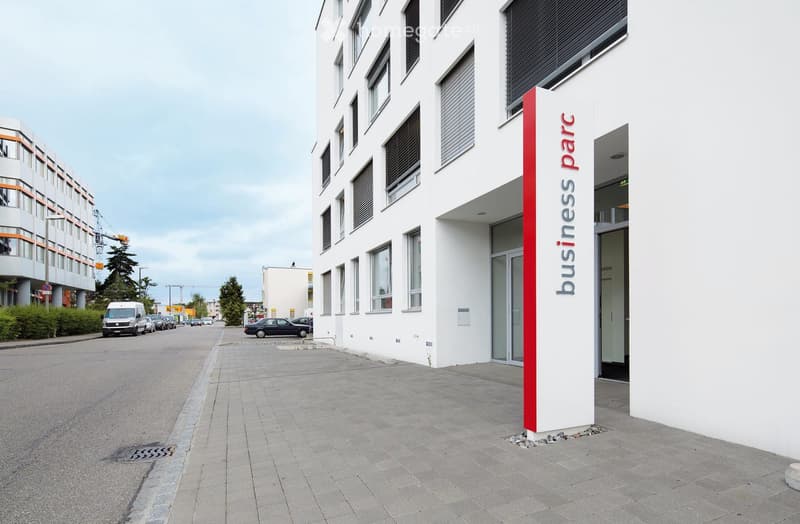 modern office building, white exterior, red and white sign, entrance on the right, paved walkway