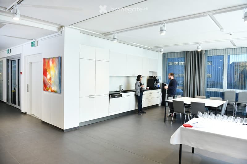 modern kitchen with large countertops, open plan with dining and sitting areas, windows, white tiled floor, a painting on the wall