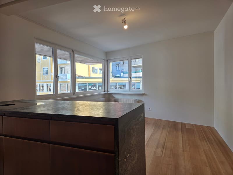 Modern kitchen with a central island, wooden flooring, and large windows offering a view of the street.