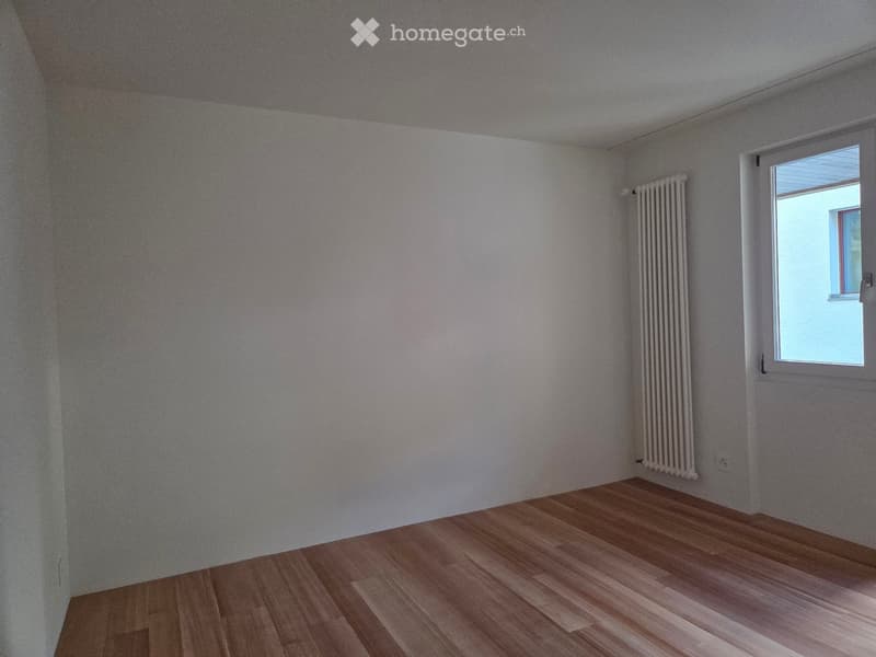 Empty room with light-colored walls, wooden flooring, and a single window with a radiator below it.