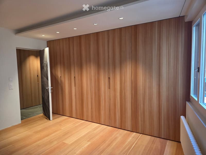 Empty room with wooden flooring, large wooden closet, and a window on the right side.