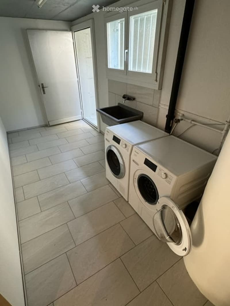 Laundry room with tiled floor, white walls, two washing machines, dryer, and a sink.