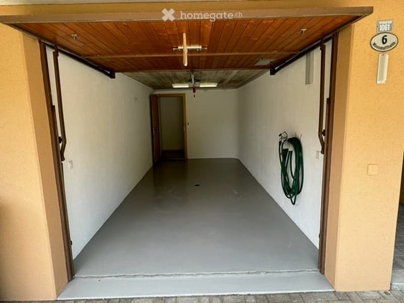 Empty garage with wooden ceiling, concrete floor, and a single door at the far end.