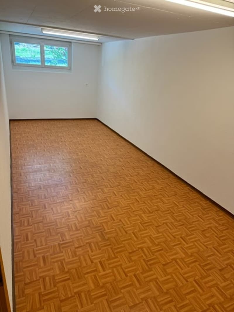 Empty room with wooden herringbone flooring, white walls, and a single window with a view of greenery.