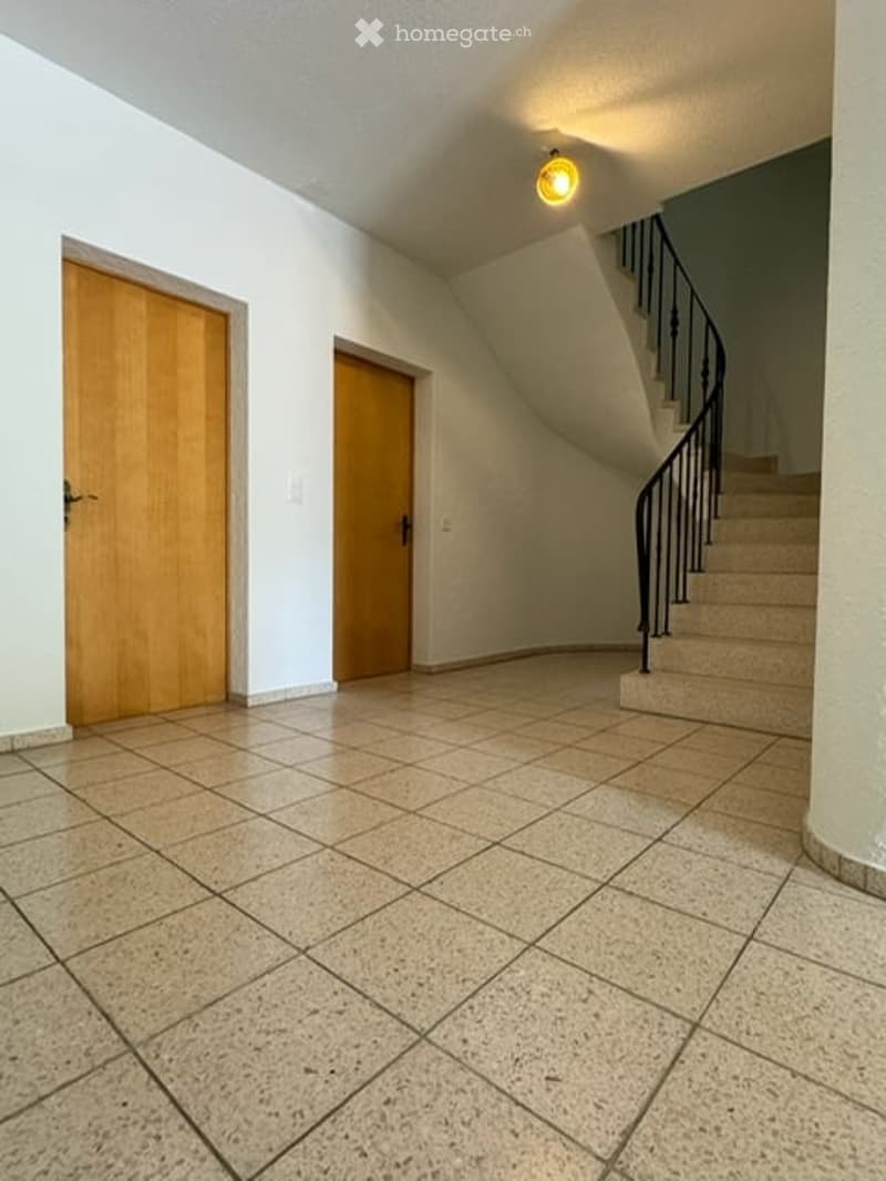 Empty hallway with tiled floor, two wooden doors, and a staircase leading upwards.