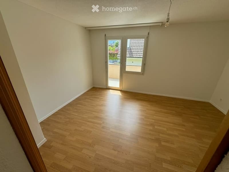 Empty room with wooden flooring, white walls, and a glass door leading to a balcony or outdoor area.