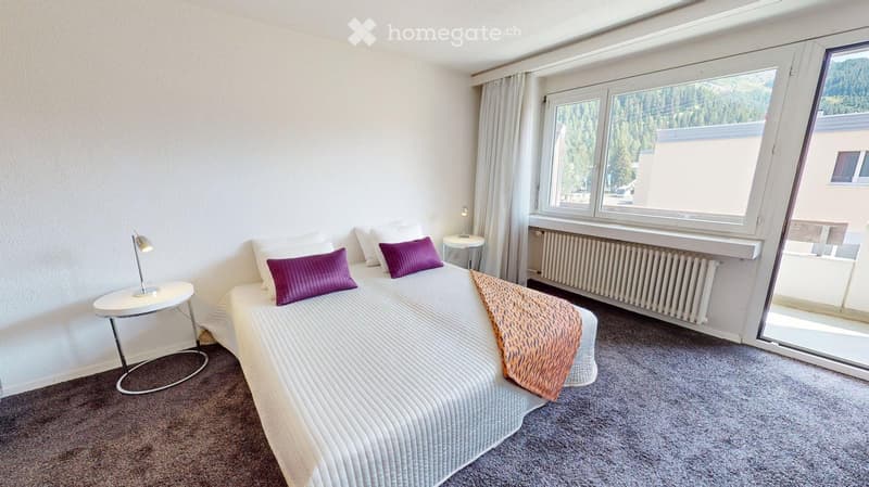 Cozy bedroom with a double bed, nightstand, and lamp. Large windows offer a scenic view of the surrounding landscape.