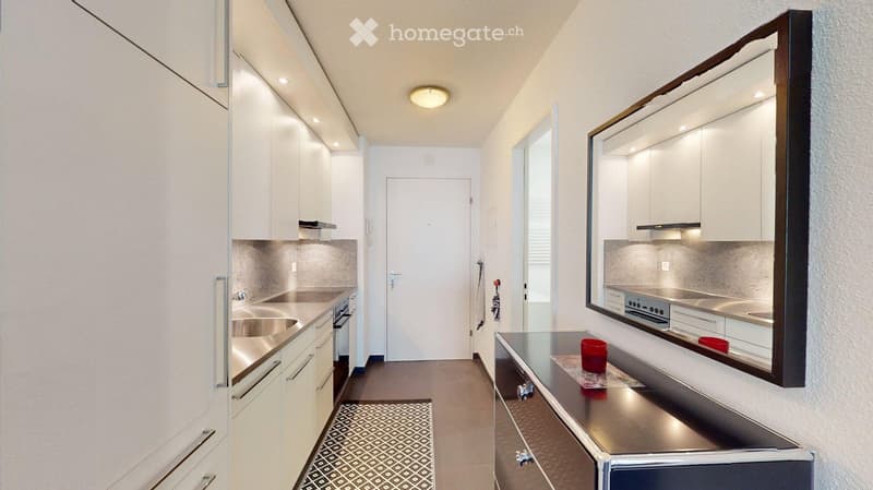 Modern kitchen with white cabinets, stainless steel appliances, and a sleek countertop. Features a built-in oven, sink, and a large mirror above the counter.
