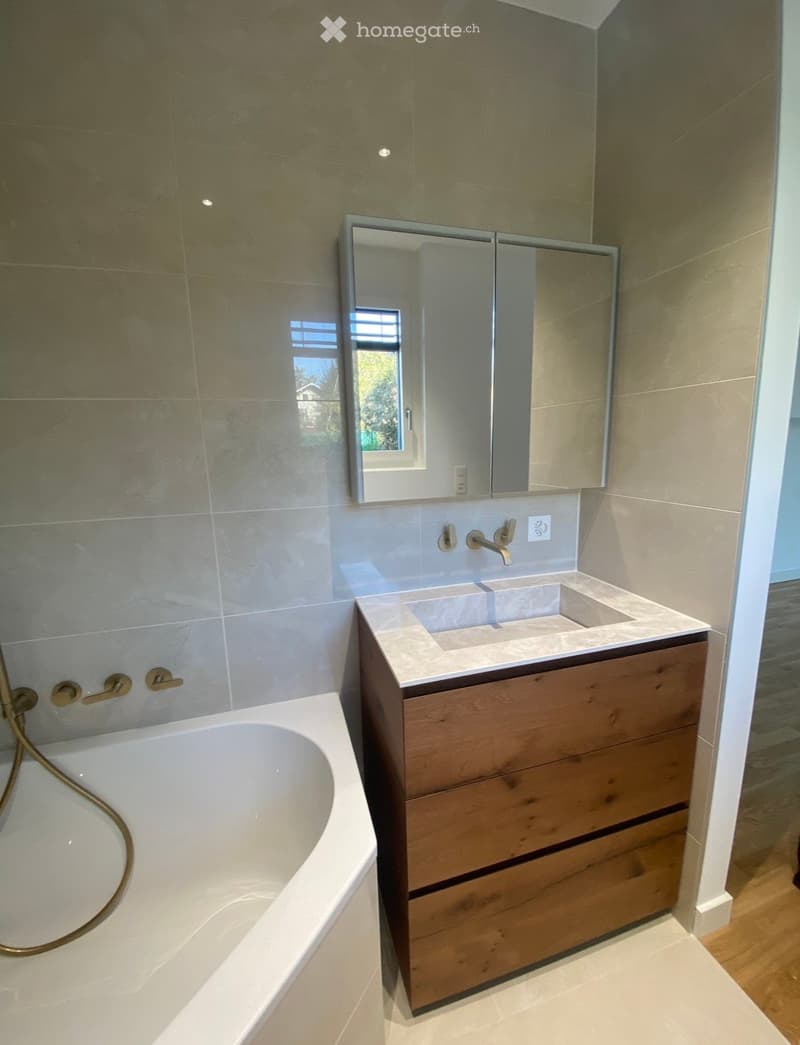 Modern bathroom with a white bathtub, wooden sink cabinet, and a large mirror above the sink.