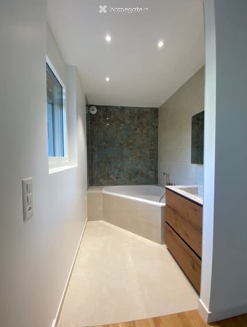 Modern bathroom with a bathtub, sink, and wooden cabinet. Features a large window and sleek, contemporary design.