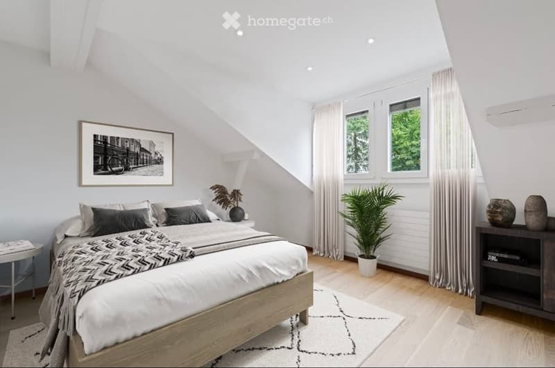 Bright, modern bedroom with wooden floors, large windows, a bed with grey and white bedding, nightstand, picture frame, potted plant, side table, and decorative vases.