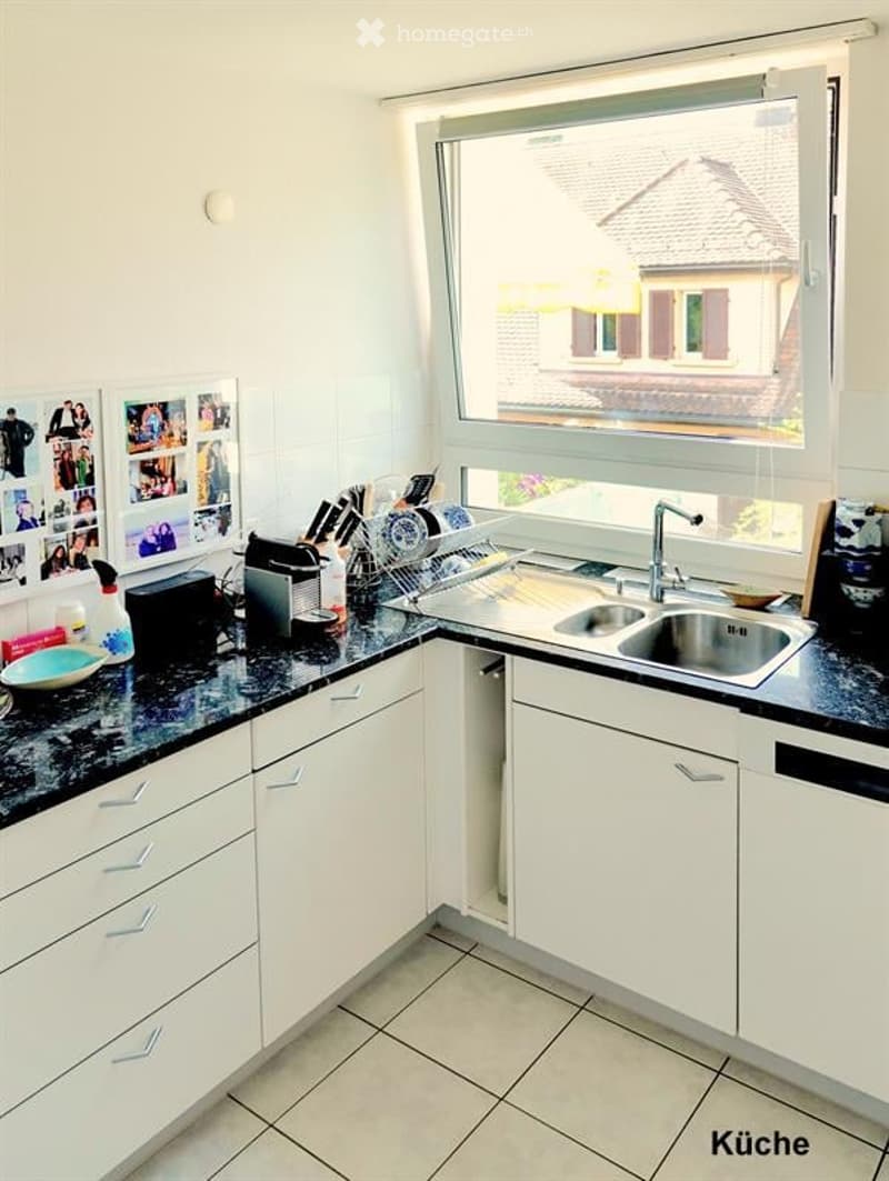 Modern kitchen with white cabinets, black granite countertops, stainless steel sink, and various appliances. A large window offers a view of the roof of a neighboring house.