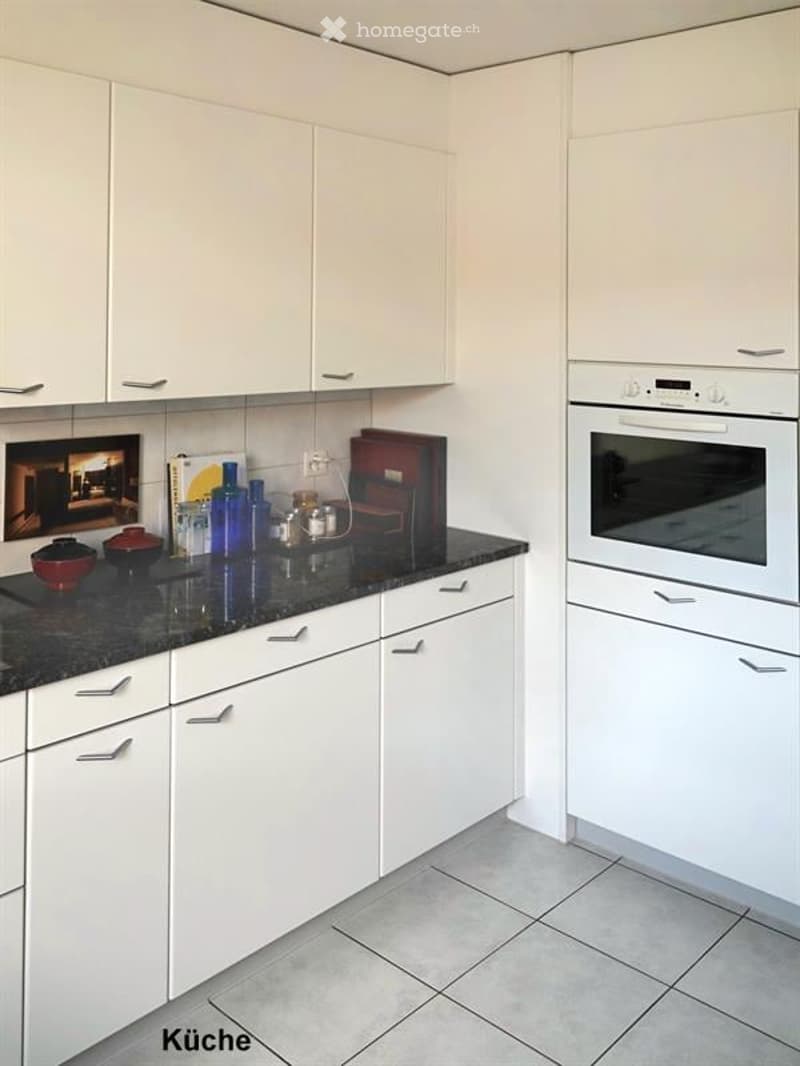 Modern kitchen with white cabinets, black granite countertop, and built-in oven. Various decorative items and containers are placed on the counter.