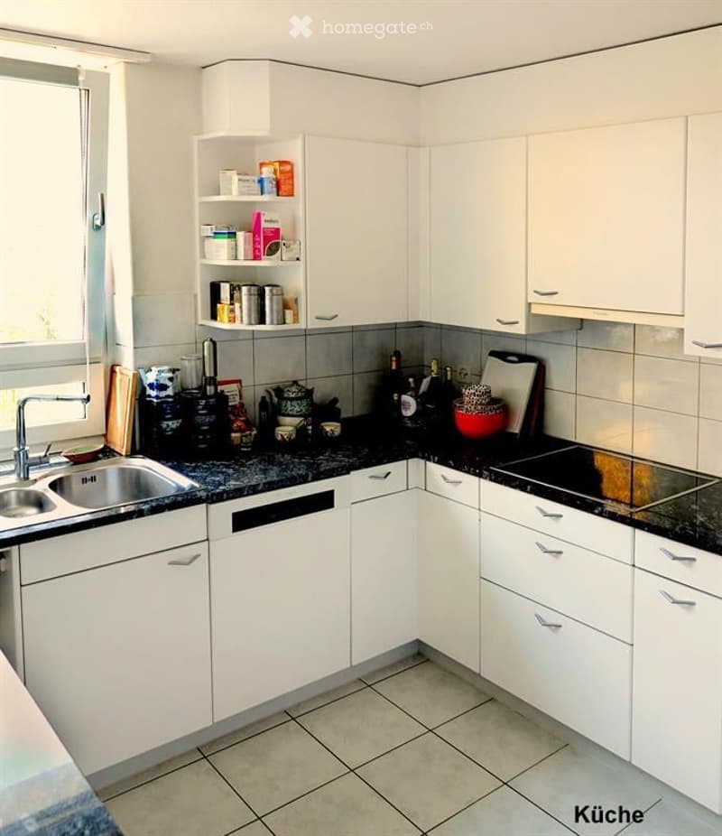 Modern kitchen with white cabinets, black granite countertops, stainless steel sink, and various kitchen items on the counter.