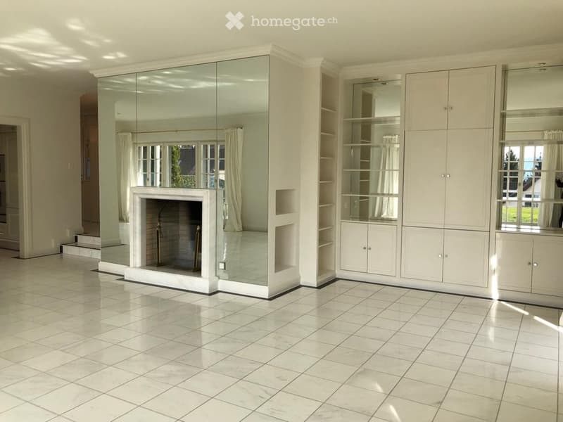 Spacious living room with a central fireplace, built-in white cabinetry, large mirrored wall, and marble flooring.