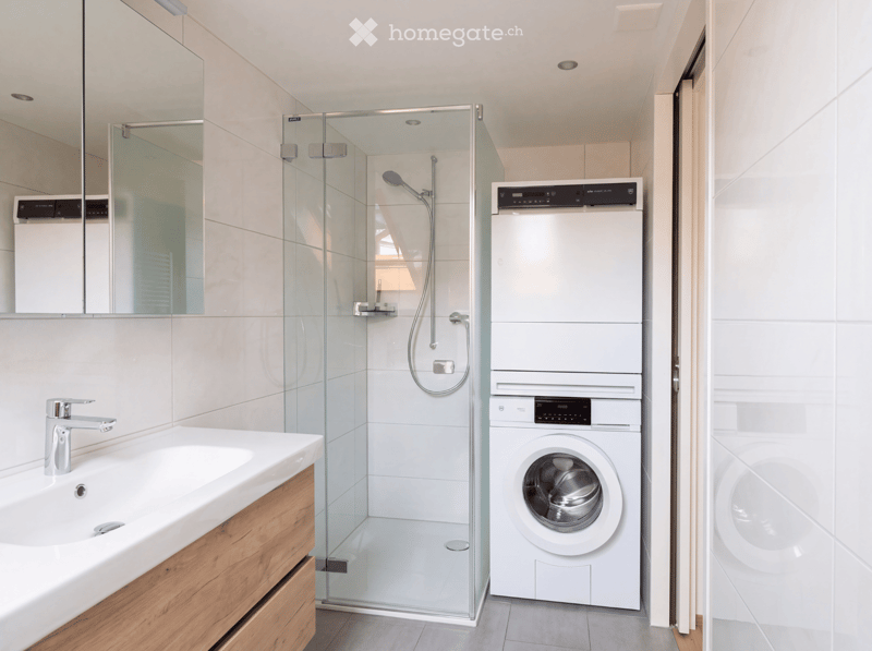Modern bathroom with a glass-enclosed shower, a sink with a wooden vanity, and a stacked washer and dryer unit.