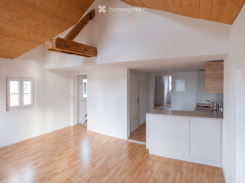 Bright, open-plan living space with wooden flooring, white walls, and a modern kitchen area featuring a kitchen island, sink, and cabinets.