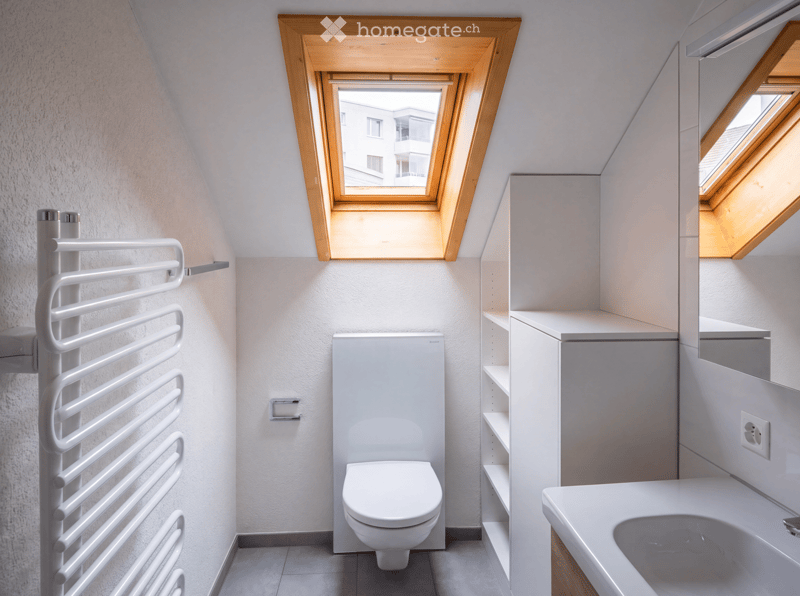 Modern bathroom with white walls, a toilet, a sink, a bathtub, built-in cabinets, and a radiator. The room features skylight windows with wooden frames.