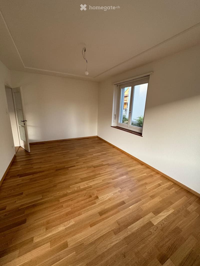 Empty room with wooden flooring, white walls, and a single window with a view of the outside. The room has a simple, clean design with no furniture or decorations.