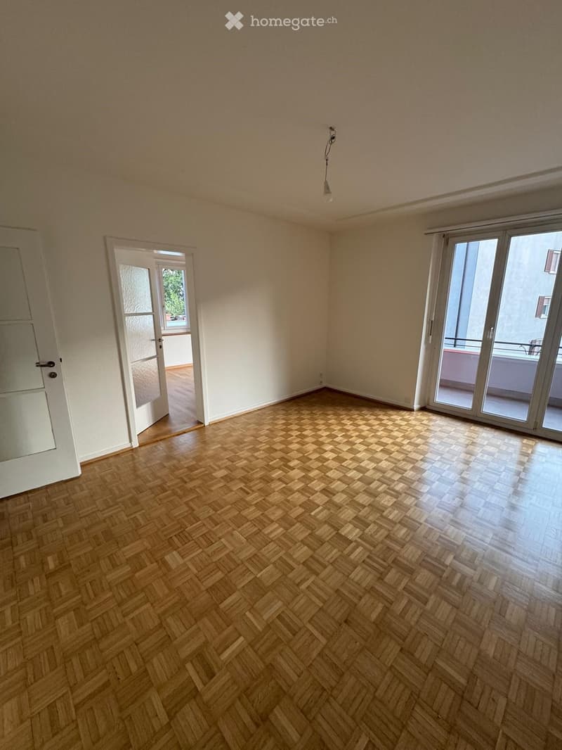 Empty room with wooden herringbone flooring, white walls, and large sliding glass doors leading to a balcony.