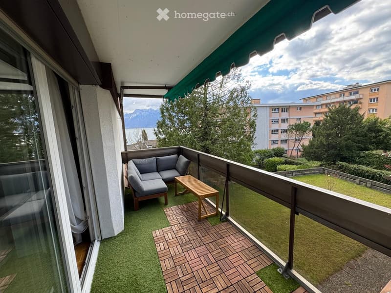 Balcony with green artificial turf, wooden decking, grey sofa, and small wooden table.