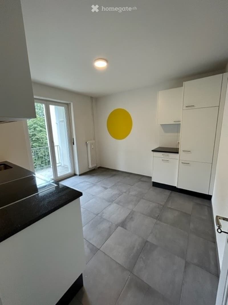 Modern kitchen with white cabinets, dark countertops, tiled floor, and a large window leading to a balcony.