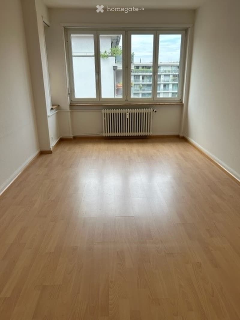 Empty room with wooden flooring, large windows, radiator, and white walls.