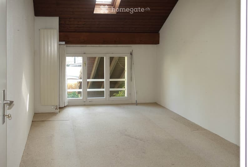 Empty room with white walls, carpeted floor, large window with blinds, radiator, and a door with a silver handle.