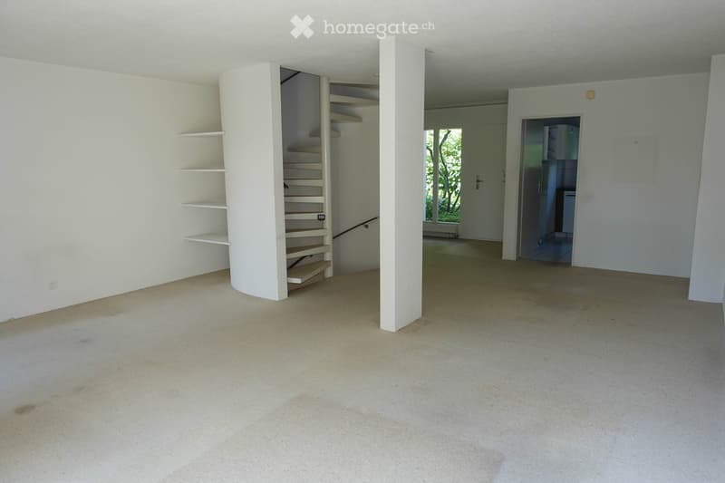 Empty room with white walls, carpeted floor, and a staircase leading to another level. There are built-in shelves on one wall and a doorway to another room.