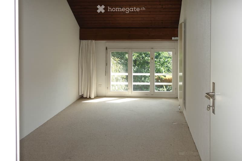 Empty hallway with white walls, carpeted floor, large window with white frame and curtains, wooden ceiling, and a door on the right side.