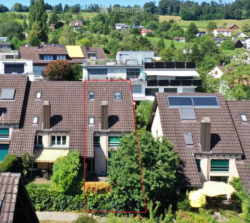 Aerial view of a residential area with multiple houses, featuring tiled roofs, solar panels, and surrounding greenery.