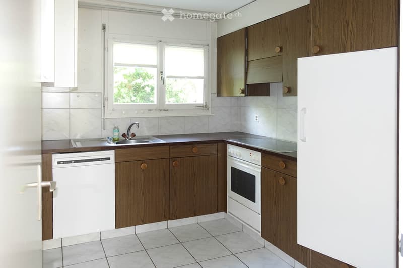 Modern kitchen with wooden cabinets, white appliances, and a large window. Includes a sink, faucet, oven, dishwasher, and refrigerator.