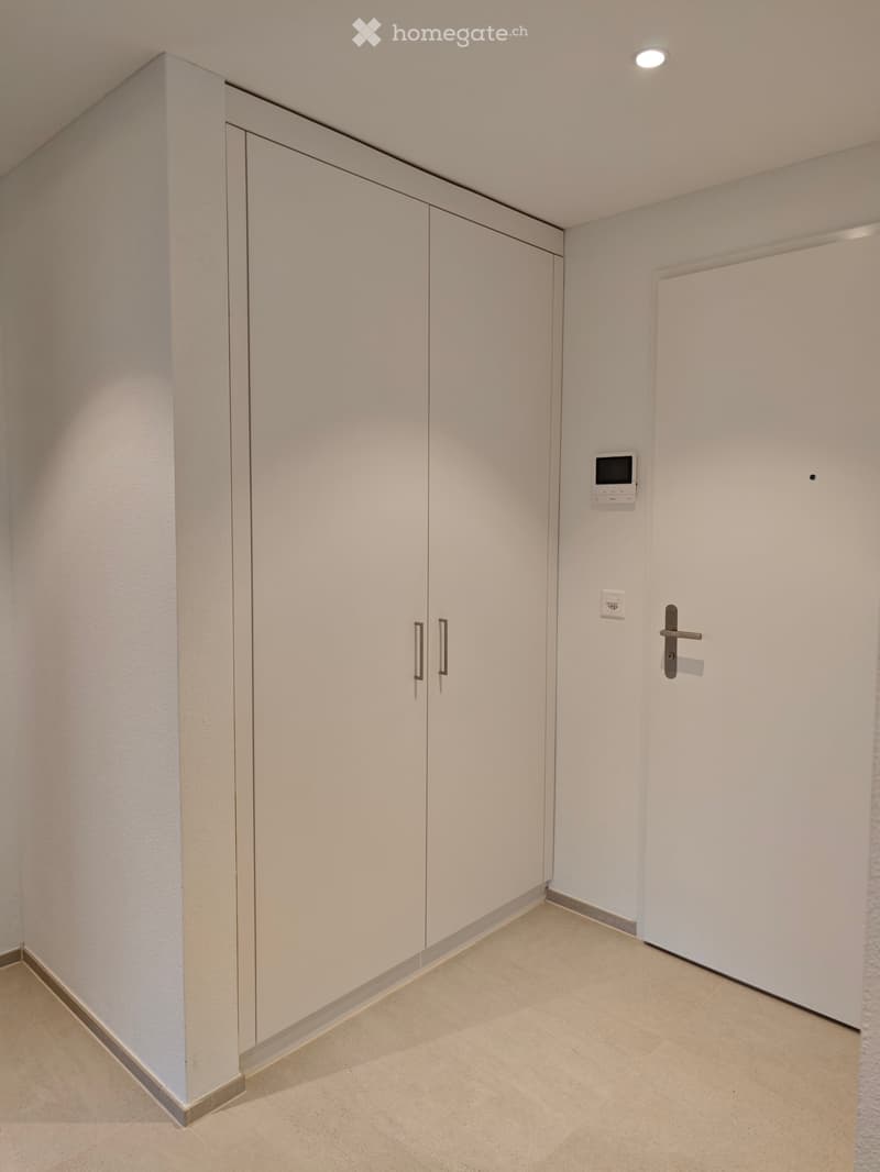 Empty hallway with white walls, beige tiled floor, built-in white storage cabinets, and a closed door.