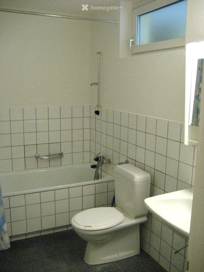 A small bathroom with a bathtub, toilet, and sink, featuring tiled walls and a window for natural light.