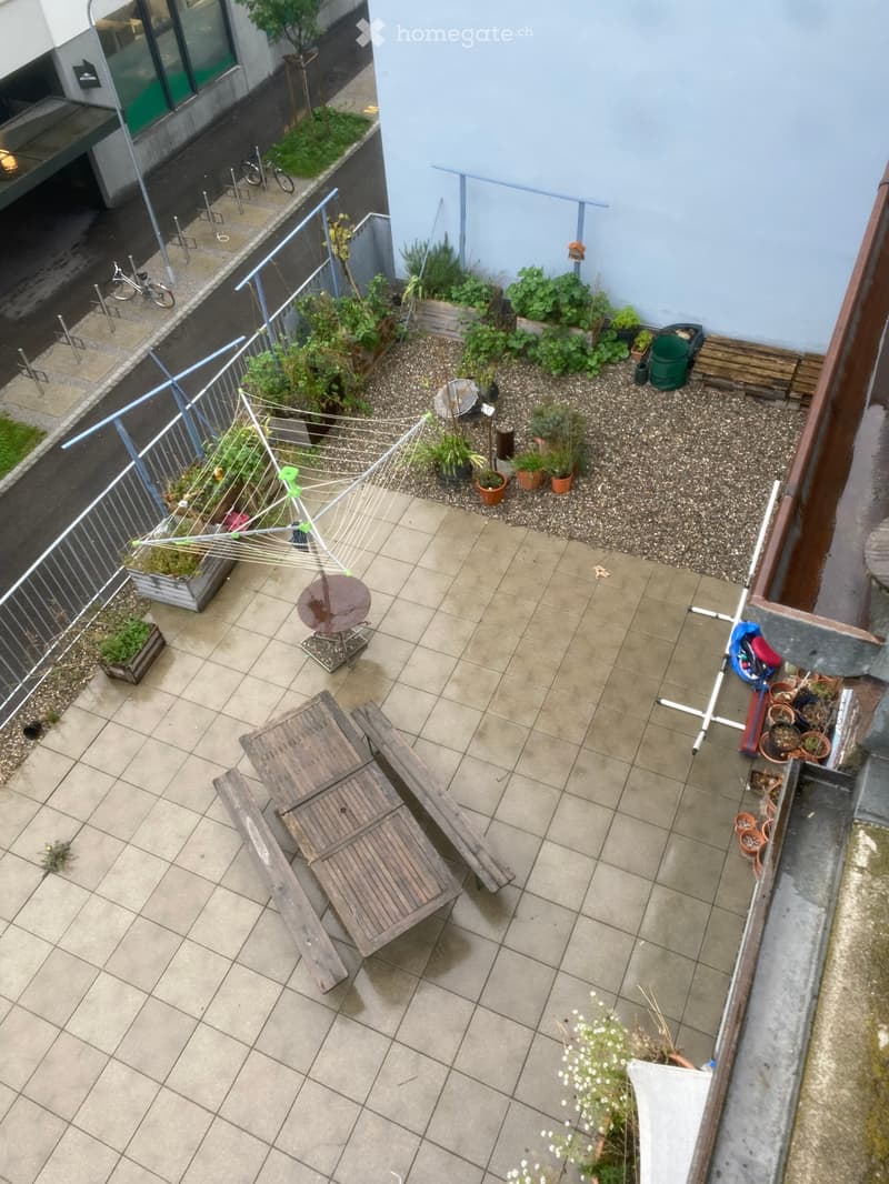 Small rooftop garden with potted plants, wooden benches, a clothesline, and a small table.
