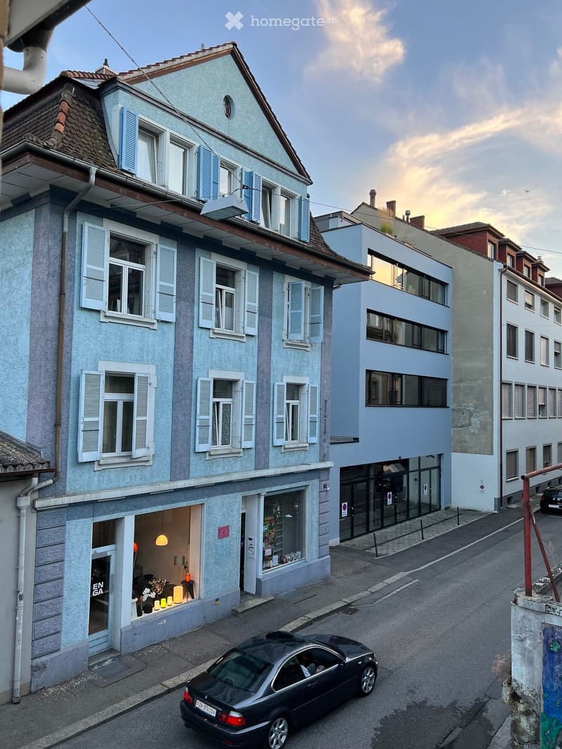 A two-story building with light blue walls and white shutters, featuring multiple windows and a small storefront with visible interior lighting and decor.