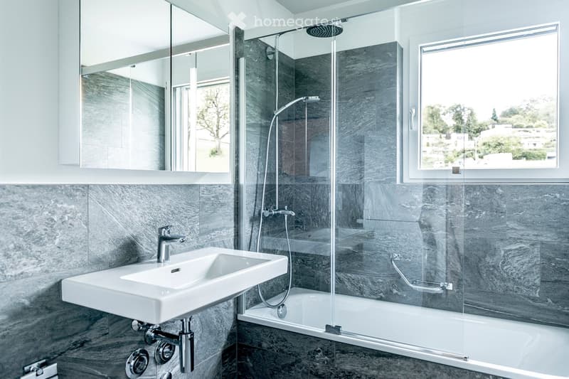 Modern bathroom with a white sink, chrome faucet, large mirror, and a bathtub with a glass shower enclosure and handheld showerhead.