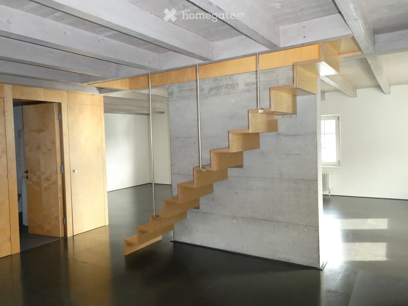 Modern hallway with a wooden staircase featuring a glass railing, concrete walls, and polished dark flooring.