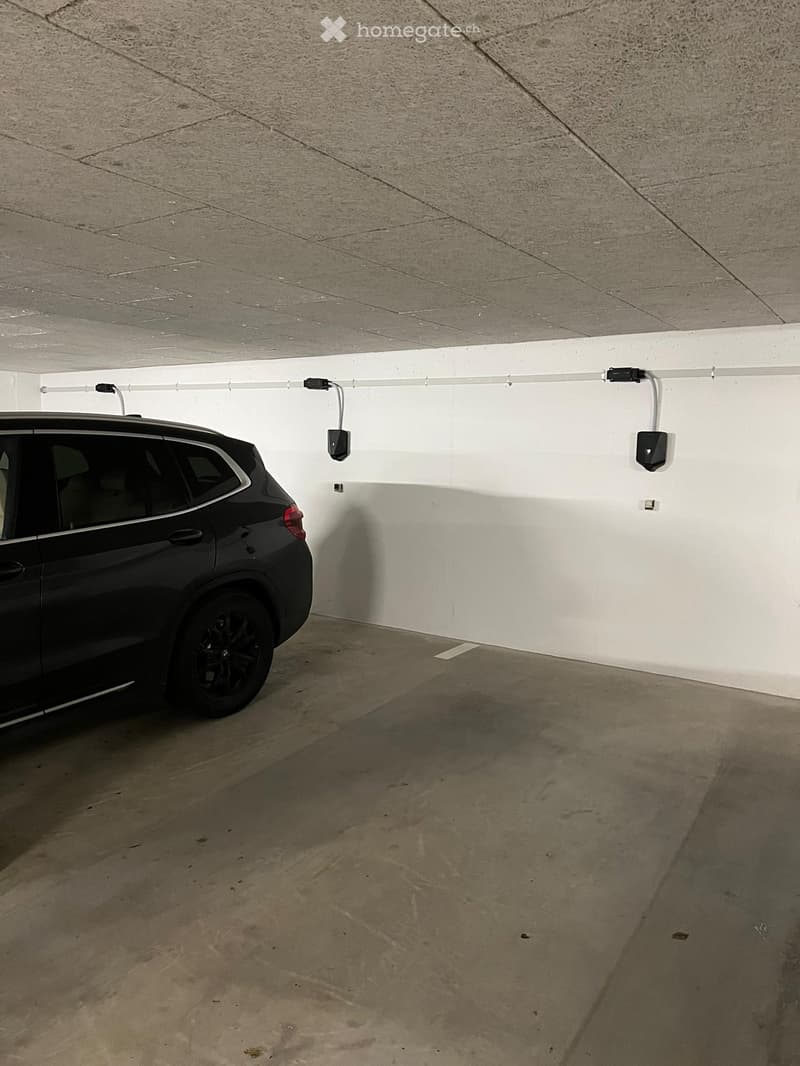 Underground parking space with a single car parked, white walls, and a concrete ceiling.