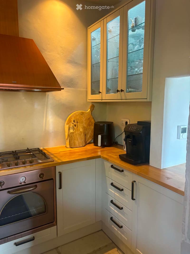 Compact kitchen with white cabinets, wooden countertops, stainless steel oven, coffee maker, air fryer, and a wooden cutting board on the counter.