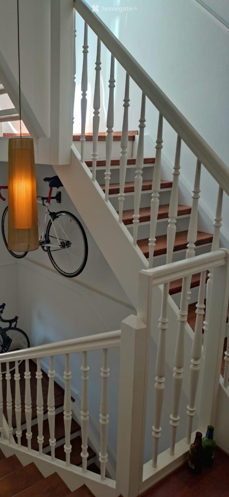 Staircase with wooden steps and white balustrade, featuring a hanging lamp and bicycles on the wall.